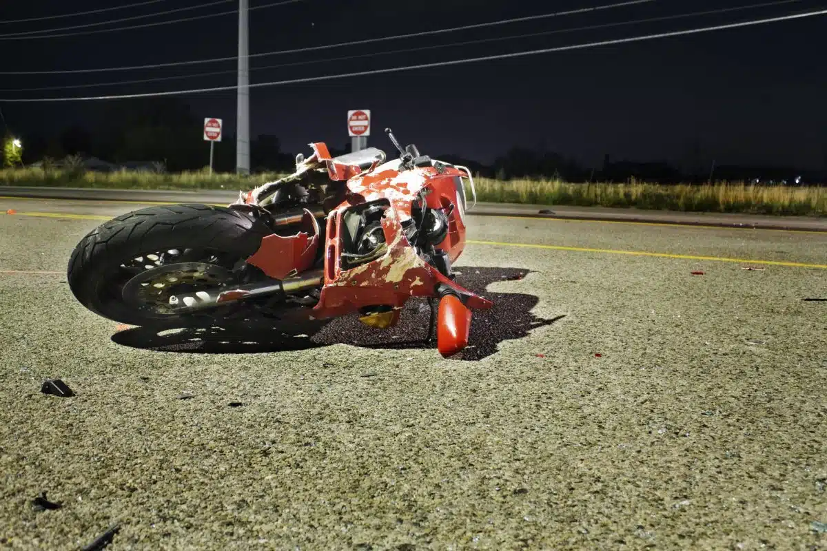 A damaged motorcycle lies in the middle of the road at night.