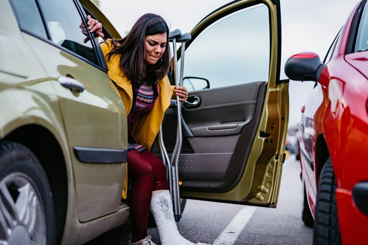 A woman with a broken leg getting out of her car on crutches.