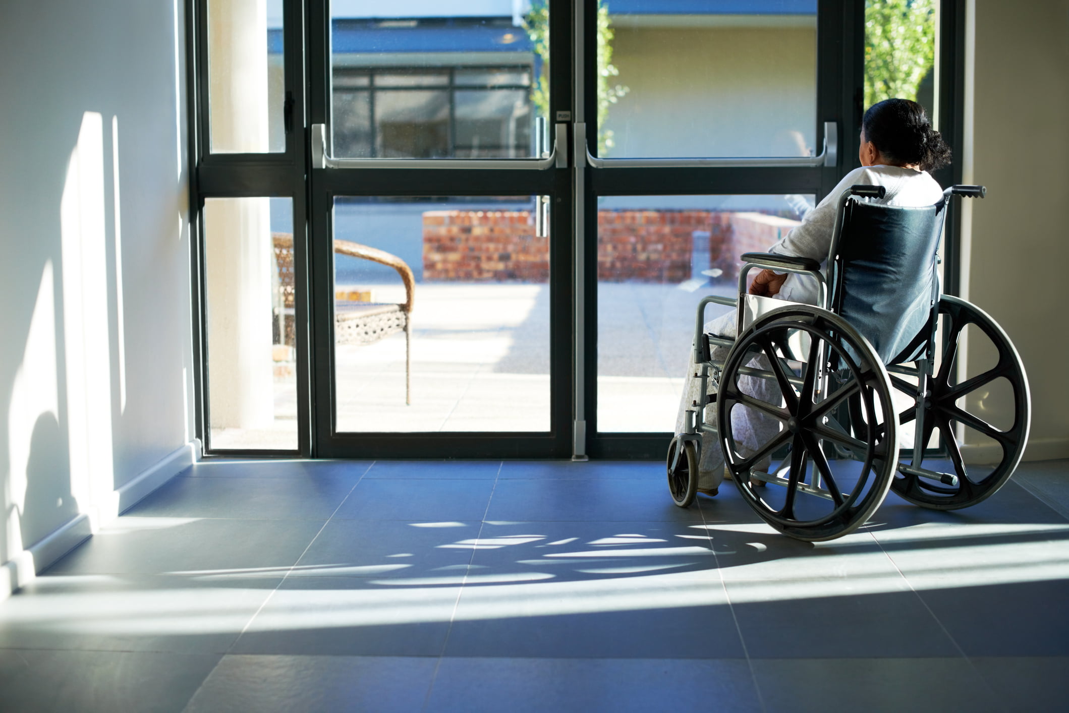 A woman in a wheelchair looks out the front door window of an assisted living facility