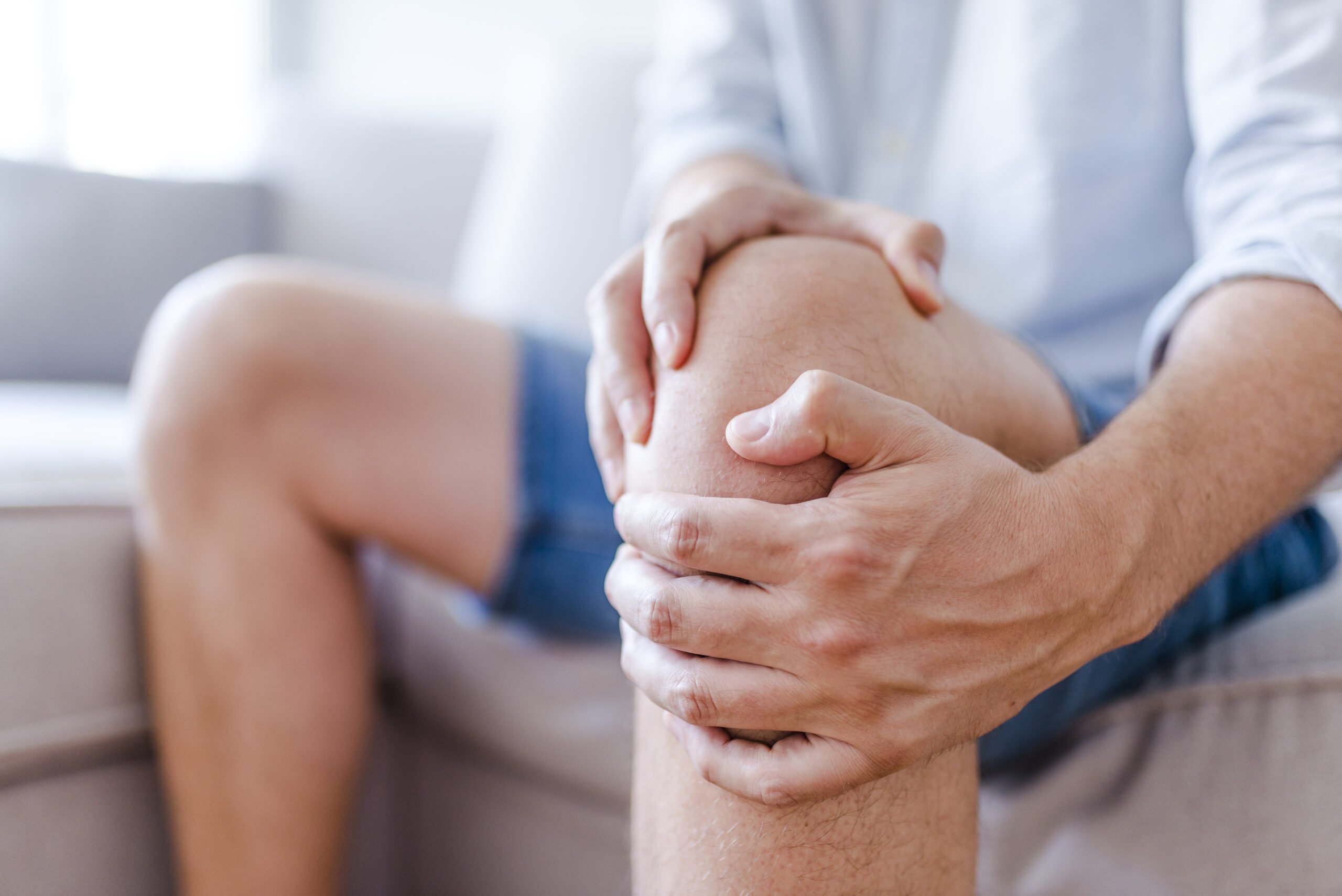 A man sits on a couch holding his knee.