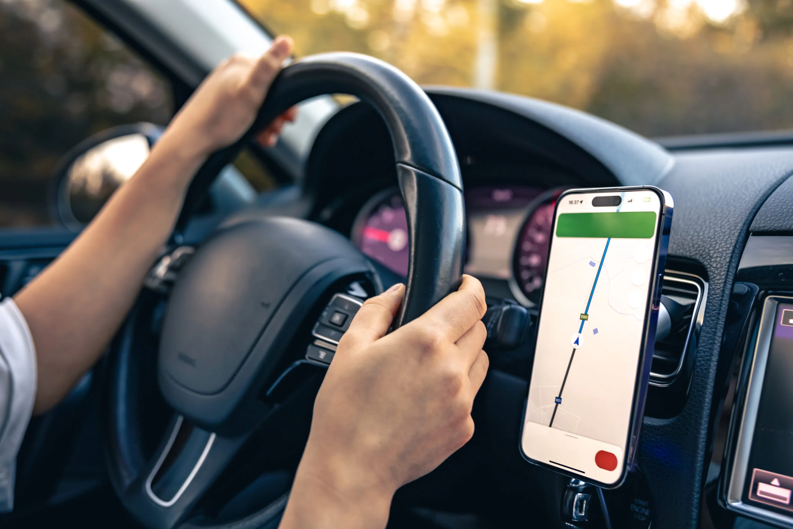 Close-up view of a driver’s GPS on their phone beside the steering wheel.