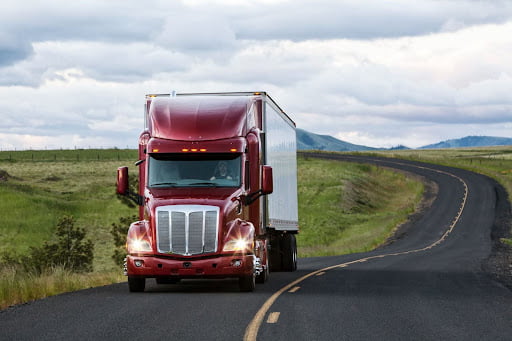 Red truck driving on a highway through the grasslands.